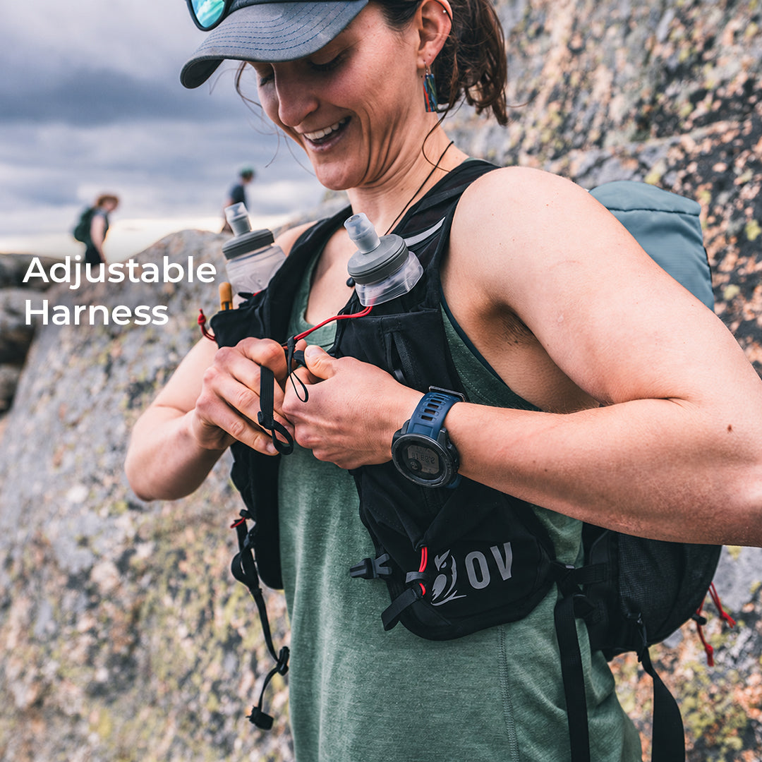 close view of hiker adjusting running vest style harness beside large rocky terrain. Text callouts say, "Adjustable Harness."
