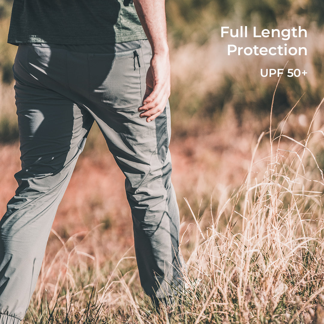 A person standing in a grassy outdoor field wearing gray full-length hiking pants, with text on the right reading 'Full Length Protection' and 'UPF 50+'.