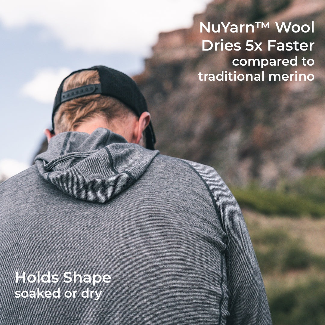 A man viewed from behind wearing a heather gray hooded top outdoors in front of a rocky cliff, with white text overlays about NuYarn Wool drying faster and holding shape.
