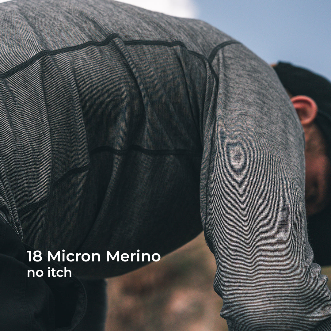 A close-up of a person wearing a long-sleeve wool athletic shirt, shown outdoors with text overlay reading '18 Micron Merino no itch'.