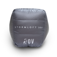 Bottom view of the red Outdoor Vitals StormLoft 30F topquilt packed inside its compression stuff sack, displaying the printed product name and OV owl logo.