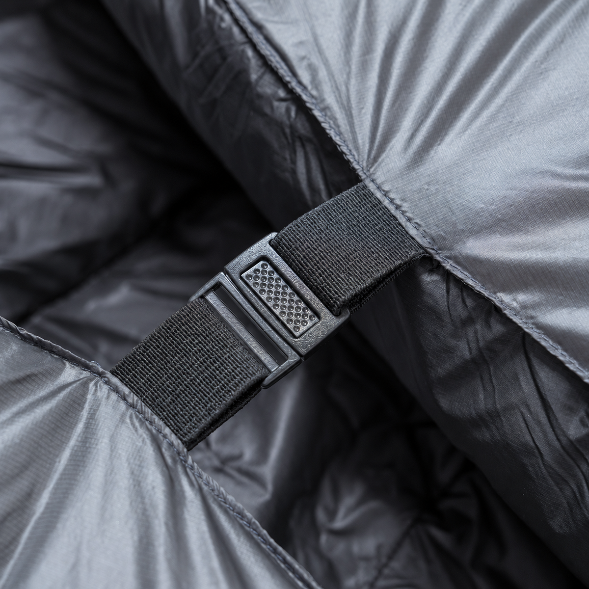 Close-up of a buckle and strap securing two sides of a backpacking quilt with a black interior together.