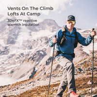 A man hiking in a mountainous outdoor setting, wearing a blue technical jacket, gray pants, a backpack, and a black cap. Text on the left reads 'Vents On The Climb Lofts At Camp' and '3DeFX™ reactive warmth insulation'.