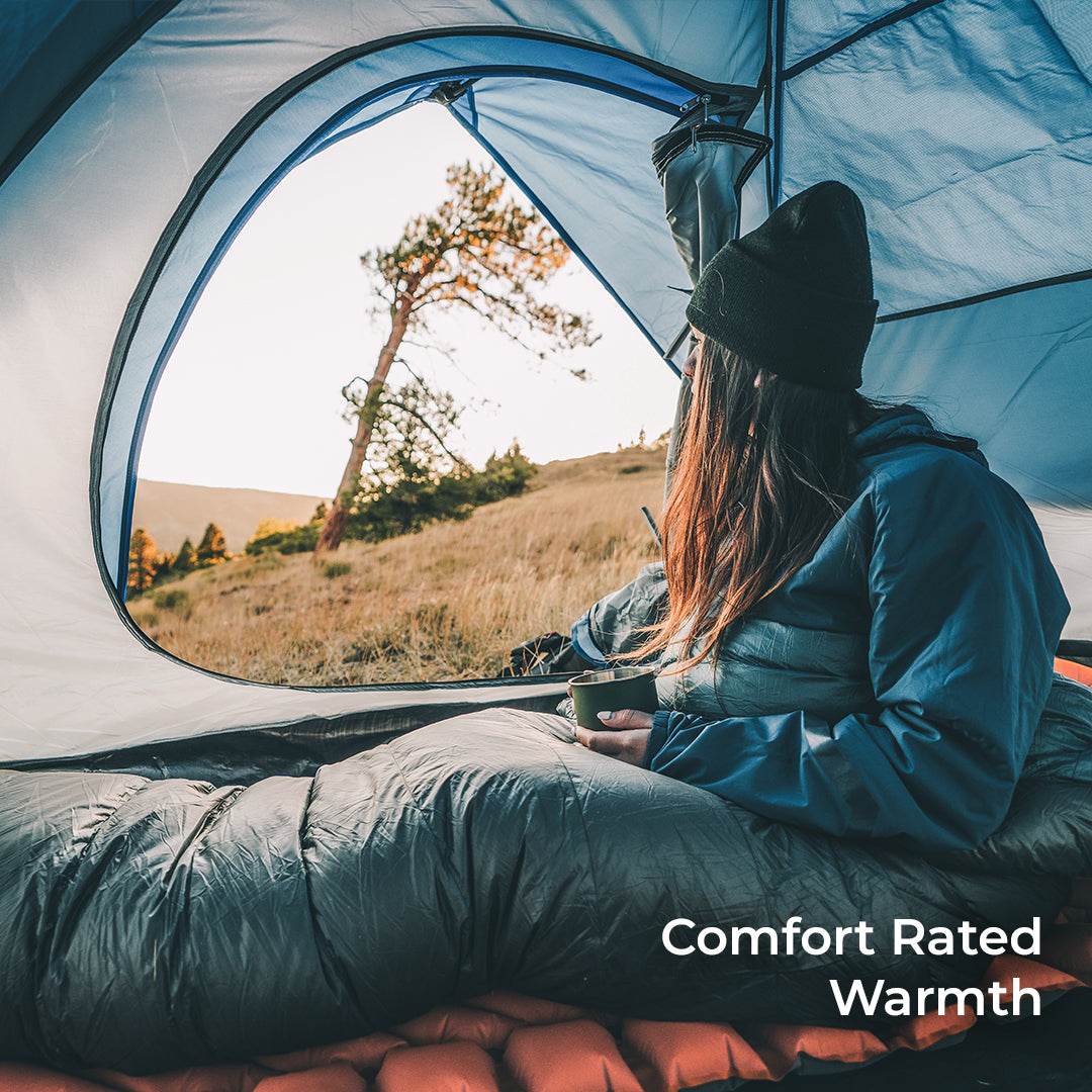 hiker sits inside blue 15 degree quilt in tent looking out the door. Callout text says, "Comfort Rated Warmth."