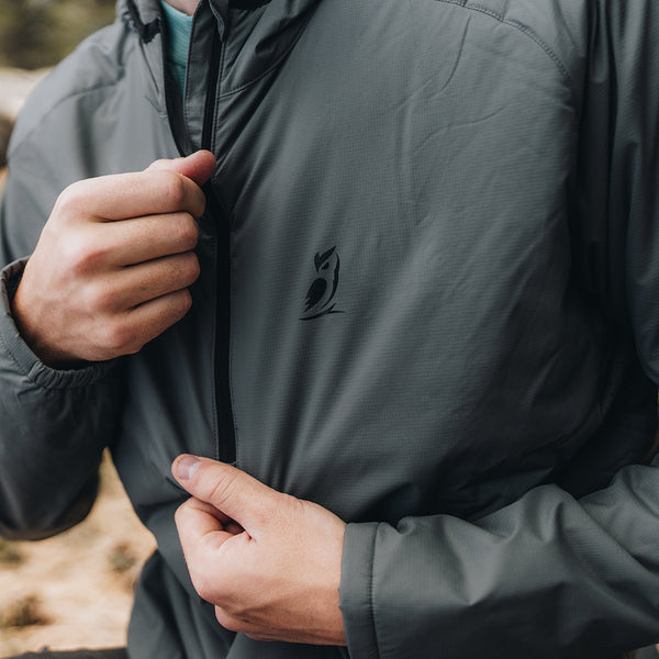 A close-up view of a person's hands holding the zipper of a Ventus Active Hoodie, showcasing the black Outdoor Vitals owl logo printed on the left chest.