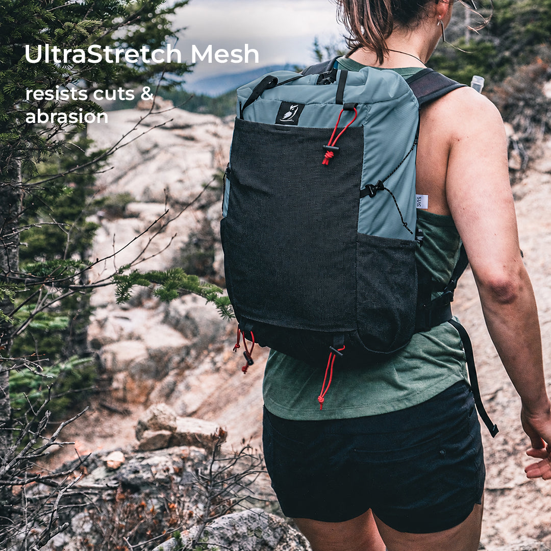 rear view of backpack on hiker in mountain terrain. Text callout says, "UltraStretch Mesh - resists cuts & abrasion."