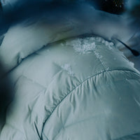 Close-up of a light gray Outdoor Vitals insulated jacket with snow resting on the shoulder and hood, showing the fabric’s weather resistance.