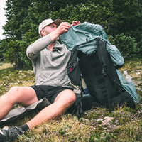 hiker removes gear from backpack while sitting on the ground near a tree