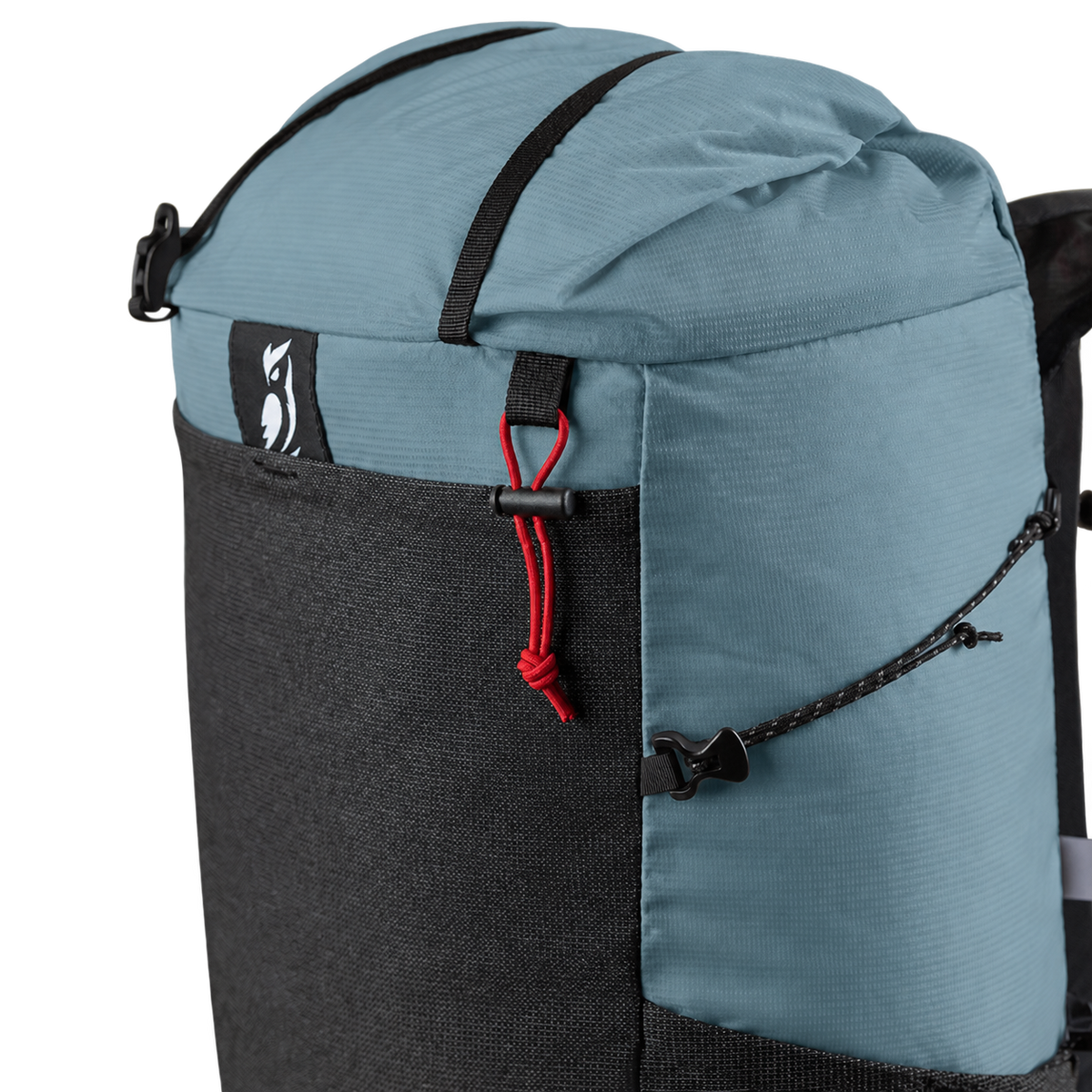Close-up of a backpack with a dusty blue top section, a black lower pocket, black straps, and a red drawcord detail on a white background.