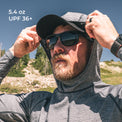 A man outdoors wearing a high-neck sun protection hooded shirt, baseball cap, and sunglasses. 
