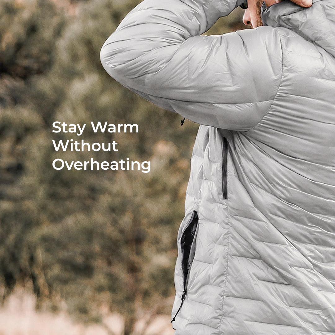 A close-up of a person wearing a light gray puffer jacket outdoors, with the text 'Stay Warm Without Overheating' overlaid on the left side.