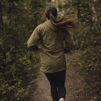 rear view of woman trail running through forest wearing green performance hoodie